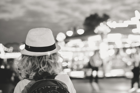 Back view of joyful cute child boy on night bokeh amuzement park outdoors background