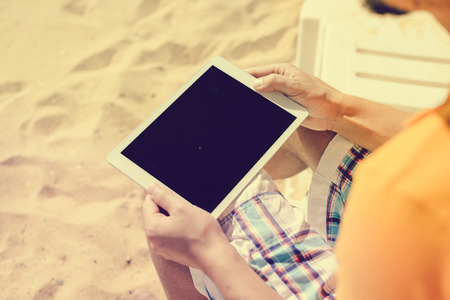 Man sitting on beach hands holding tablet