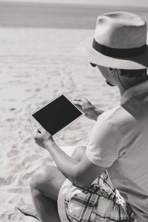 Man sitting on beach hands holding tablet