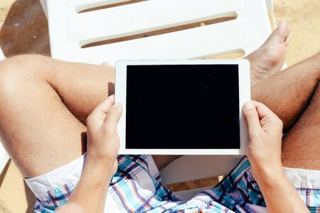 Man sitting on beach hands holding tabletの写真素材