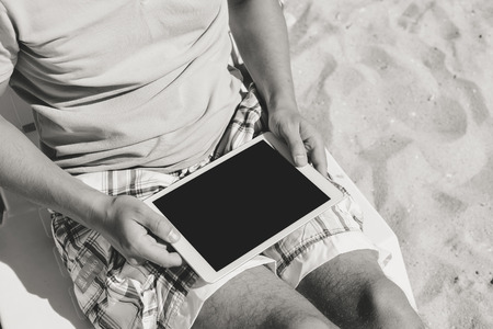Man sitting on beach hands holding tabletの写真素材