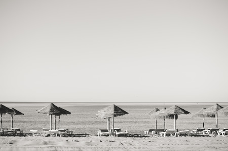 Holiday and vocation image with sandy beach, parasol and chairs on outdoors background. Black and white imageの写真素材