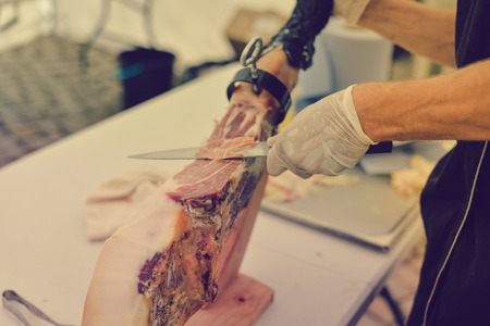 Dry cured ham thinly sliced. Closeup on chef hands in gloves slices prosciutto Italian delicatessen. Festive time backgroundの写真素材