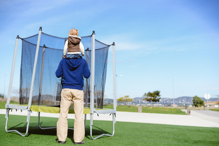 Back view of parent with child and trampoline. Family time ready for jumping on sunny day outdoors backgroundの写真素材