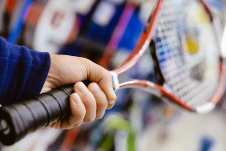 Closeup on person holding tennis racket in his hand on shopping centre backgroundの写真素材