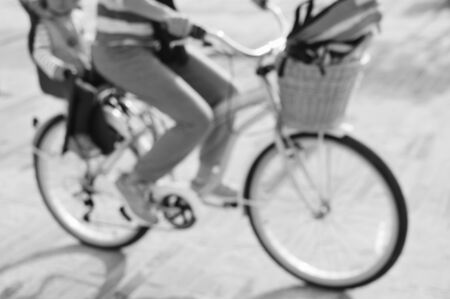 Defocused silhouette of active mother and child riding a bike together on oudroors background. Back side view blurry image travel journeyの写真素材