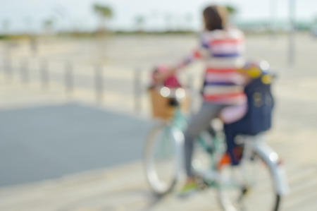 Defocused silhouette of active mother and child riding a bike together on oudroors background. Back side view blurry image travel journeyの写真素材