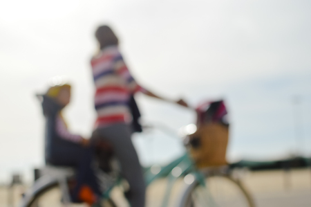 Defocused silhouette of active mother and child riding a bike together on oudroors background. Back side view blurry image travel journeyの写真素材
