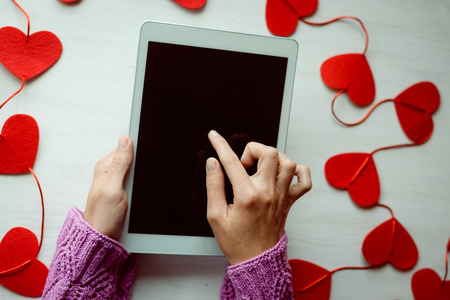 Woman hand holding using mobile smart tablet with red love hearts on table background. Top view mock up image. Valentine day feelingsの写真素材