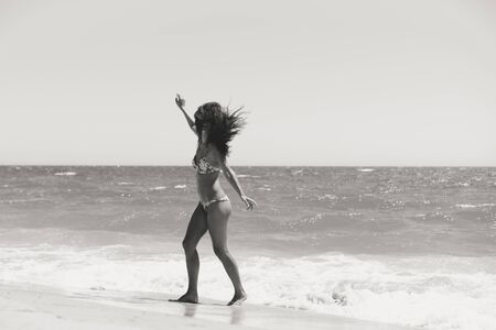 Black and white back view of beautiful woman in bikini on the sunny beach outdoors background.の写真素材
