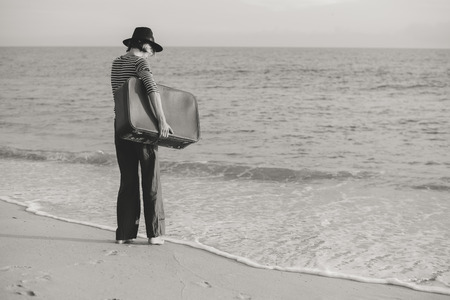 Black and white back side view image of person with suitcase on the beach outdoors backgroundの写真素材