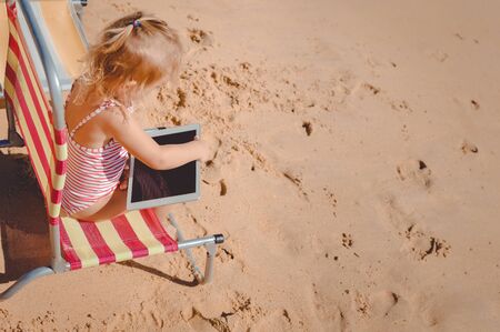 Little girl cute blond kid using tablet pc computer on sunny beach travel outdoor background. Top side view mockup style designの写真素材