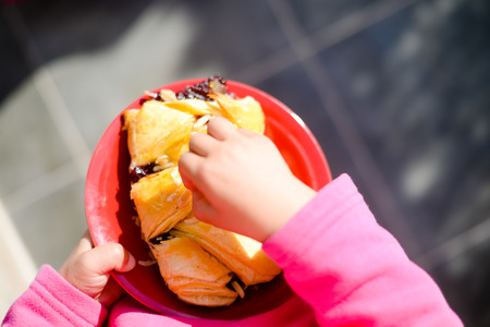 Child holding pastry on the red plate background. Closeup top side view imageの写真素材