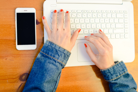 Woman hands working using computer and mobile phone. Closeup view of mock up smartphone display network connection on table backgroundの写真素材