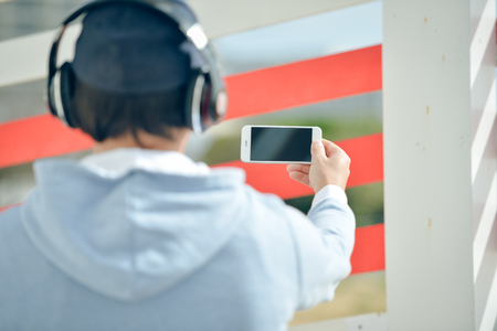Back view of man with headphones holding mobile smart phone on outdoors backgroundの写真素材