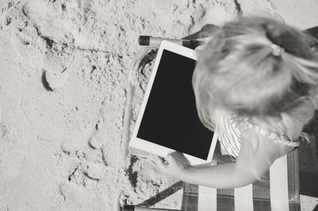 Albufeira, Portugal - 10 October, 2016: Child holding in hands Apple Ipad 2 tablet computer on beach outdoors background. Vacation relaxation closeup shot. Mobility e-reader, smart pad on chairのeditorial素材