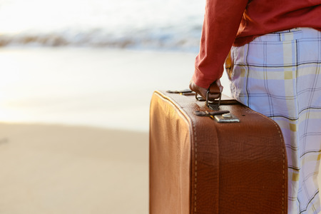 Summertime tourism. Man holding luggage on the beach sunny day outdoor backgroundの写真素材