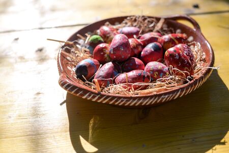 Colorful Easter eggs on ceramic plate wooden table background. Seasonal traditional handmade religious decorationの写真素材