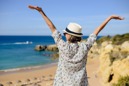 Back view of joyful amazed woman looking at the ocean natural outdoors background. Nice sunny morning seasonal travel vacation walk. Relaxing lifestyleの写真素材