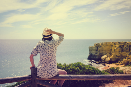 Back view of joyful amazed woman looking at the ocean natural outdoors background. Nice sunny morning seasonal travel vacation walk. Relaxing lifestyleの写真素材