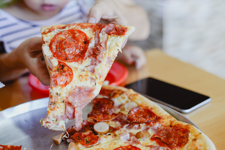 Closeup of people eat and work. Hands, sliced pizza and using smartphone on restaurant table background. Communication, friendship leisure lifestyleの写真素材
