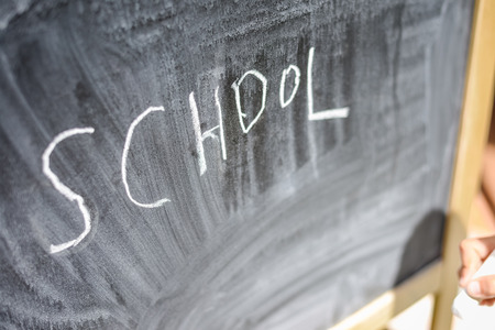 Kid's hand holding a chalk on the chalkboard grungy background. Closeup photographyの写真素材