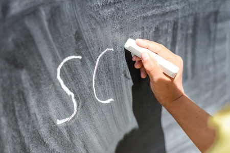 Kid's hand holding a chalk on the chalkboard grungy background. Closeup photographyの写真素材
