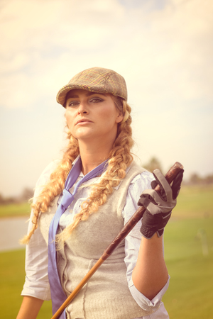 Portrait of cheerful caucasian woman holding golf club on green field outdoor backgroundの写真素材