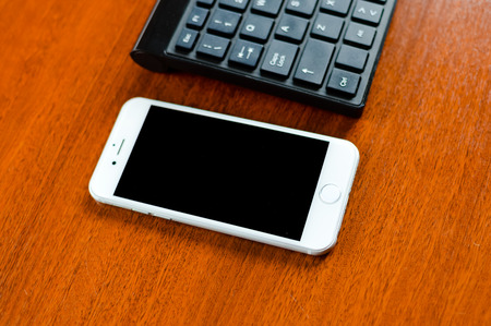 Lisbon, Portugal - March 23, 2017: Closeup on Apple iPhone 7 smartphone and computer pc keyboard on light table background. Mock up black display copy space, flat lay top side viewのeditorial素材