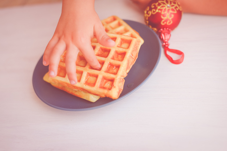 Closeup of child hand and baked waffles on light table background. Top side view on tasty natural decoration. Xmas classic lifestyle. Winter style delicious pastries.の写真素材