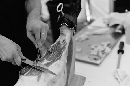 Dry cured ham thinly sliced. Closeup on chef hands in gloves slices prosciutto Italian delicatessen. Festive time backgroundの写真素材