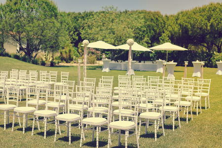 Beautiful arrangement for wedding ceremony event on the natural outdoors lawn park background. Flowers, tables, chairs, elegant romantic decoration details and luxury gathering lifestyleの写真素材