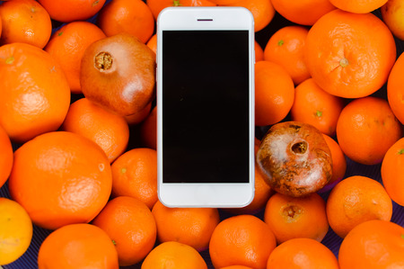 Closeup of mobile phone over fresh orange fruits background. Mockup flat lay digital communication technology design healthy natural dietの写真素材