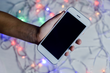 Hand holding mobile smart phone over led lights on a wooden texture background.の写真素材