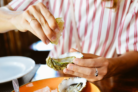 Close up on hand of a woman holding oyster, ice and lemon on platter wooden table background.の写真素材