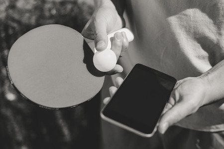 Closeup on person hand using smartphone with black screen and ping-pong racket on blue sky backgroundの写真素材