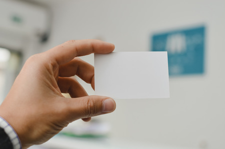 Close up on hand of a person holding showing white business card over blurry office backgroundの写真素材