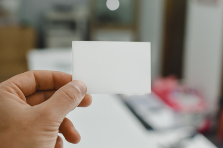 Close up on hand of a person holding showing white business card over blurry office backgroundの写真素材