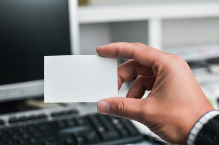 Close up on hand of a person holding showing white business card over blurry office backgroundの写真素材
