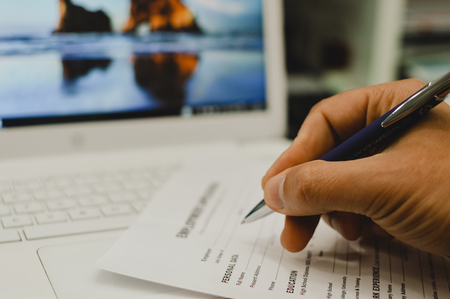 Closeup of hand writing filling job or service application form over light desk background. Signing with pen checklist, college student or education university program certificate. Business contractの写真素材