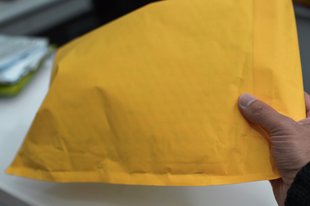 Closeup on hand with letter craft envelope on the background. Receiving and sending commercial or personal package, top view communication conceptual designの写真素材