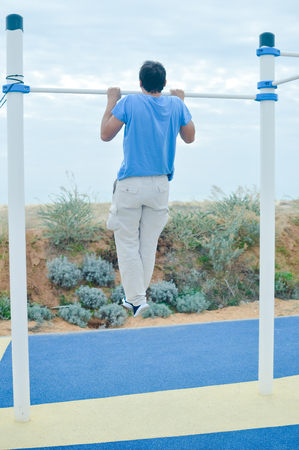 Outdoors fitness training active lifestyle, back view of man doing sport exercising on horizontal bar in summer park sky backgroundの写真素材