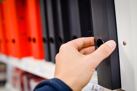 Close up on hand holding office folders on the bookshelf backgrounds.の写真素材