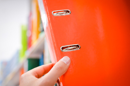 Close up on hand holding office folders on the bookshelf backgrounds.の写真素材