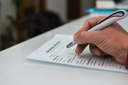 Closeup on hand of a person signing document contract form on light table backgroundの写真素材