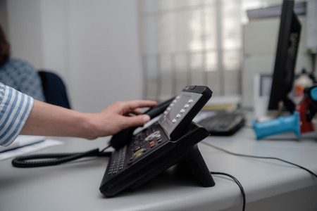 Closeup of businesswoman dialing making office phone-call, light table background. Corporate female holding telephone handle digital electronic pc connection checking daily data news, online talk jobの写真素材