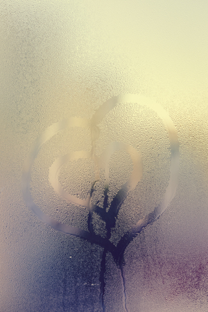 Love heart sign and foggy condensated window with blurry effect textured outdoors background, close up imageの写真素材