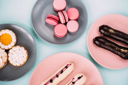 Macaroons, eclairs and tarts flatlay. Blue background.
