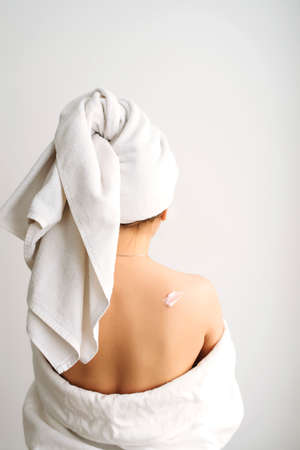 Woman in white towels after bath applying cream or lotion on her back. Skin care concept.の写真素材