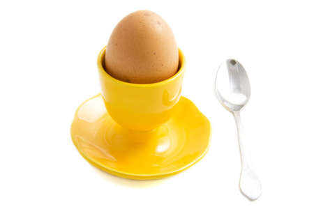 Egg in yellow egg cup with silver spoon isolated over whiteの写真素材